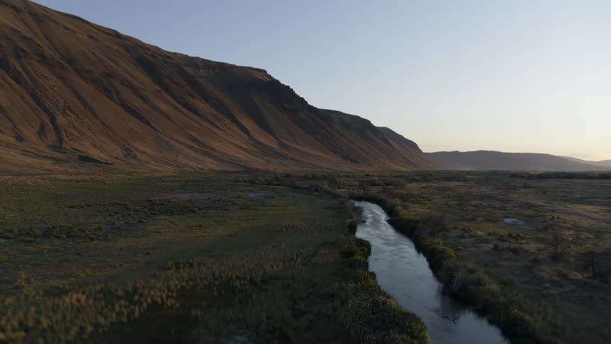 Pullback reveal over a reflective stream that winds along a dramatic mountain valley at sunset