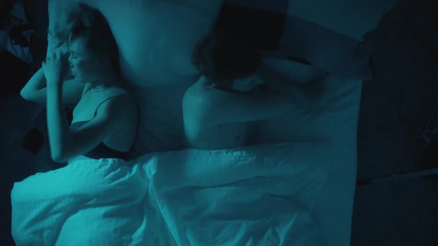 A husband and wife cuddling while sleeping in bed at night