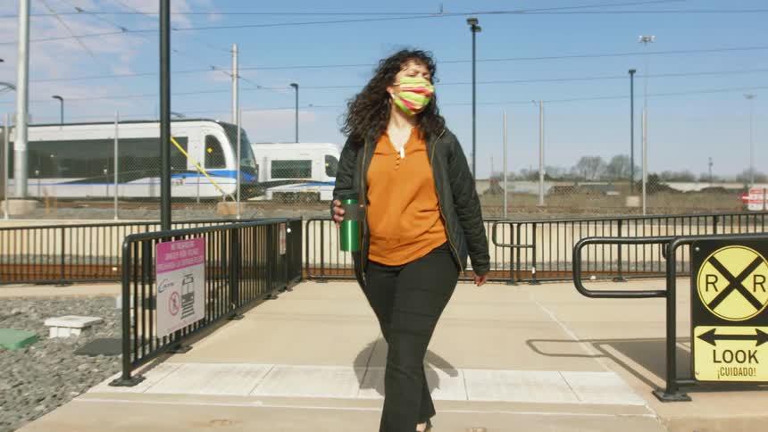 A woman with a mask walking with trains train tracks the sky and clouds in the background