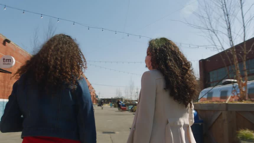 Two women wearing face masks walk past outdoor seating of cafe and other businesses