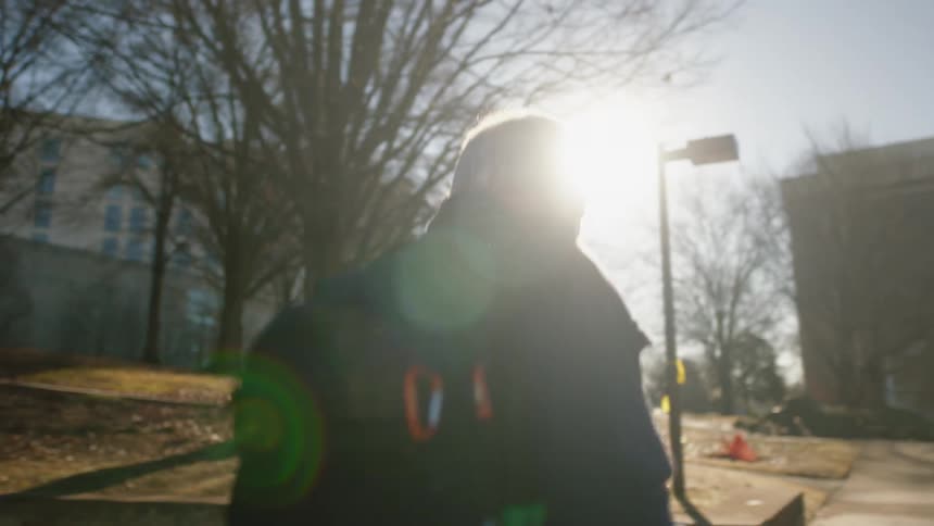 A professor walks through campus with a backpack slung over his shoulder