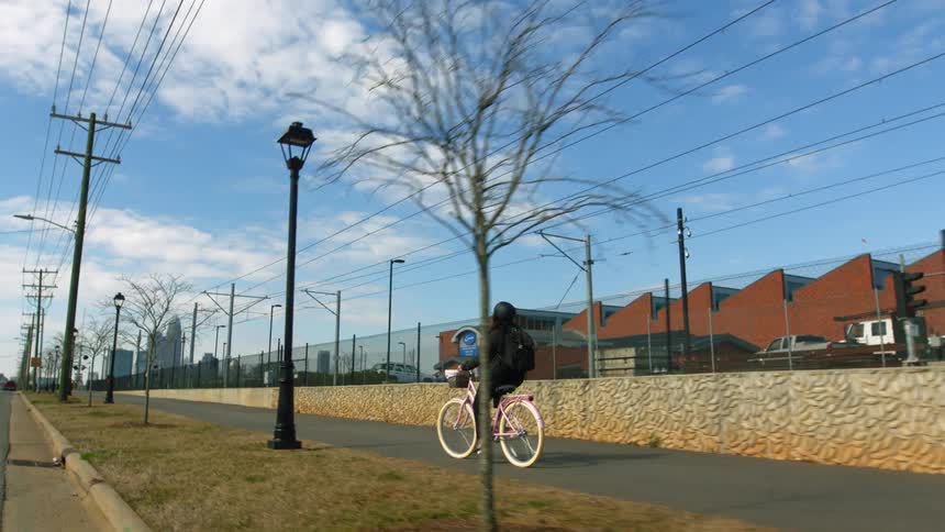 A person rides a bike down a sidewalk past buildings behind a fence