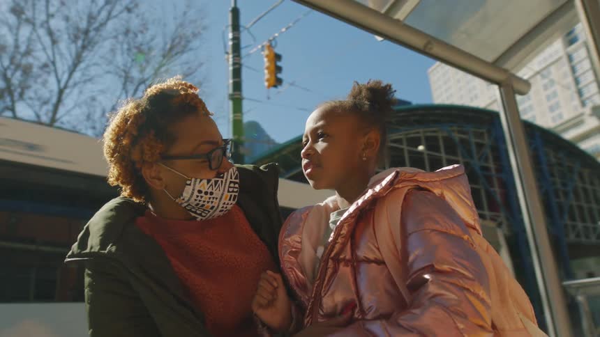 A mother and young daughter talking while waiting at a city bus stop