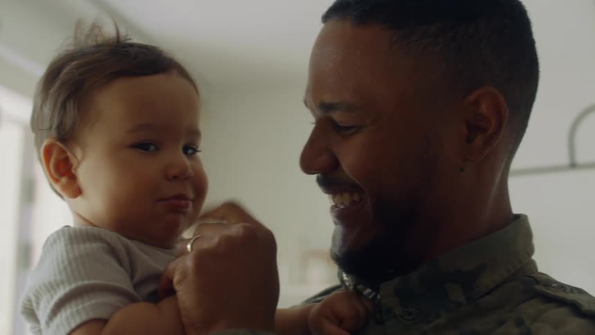 A father smiling while holding a baby and running his finger over its lips