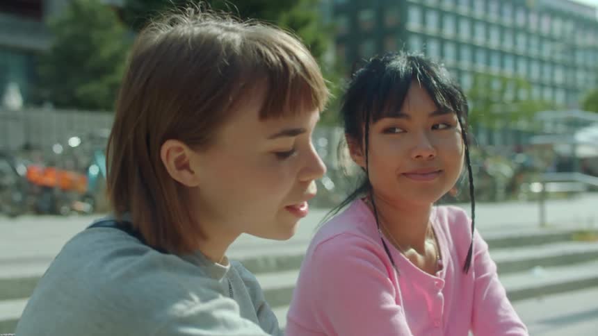 Two women are sitting on some steps and one helps the other get a hair out of her eyes