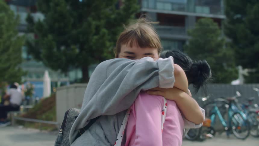 A woman surprising another woman before both walking away talking happily