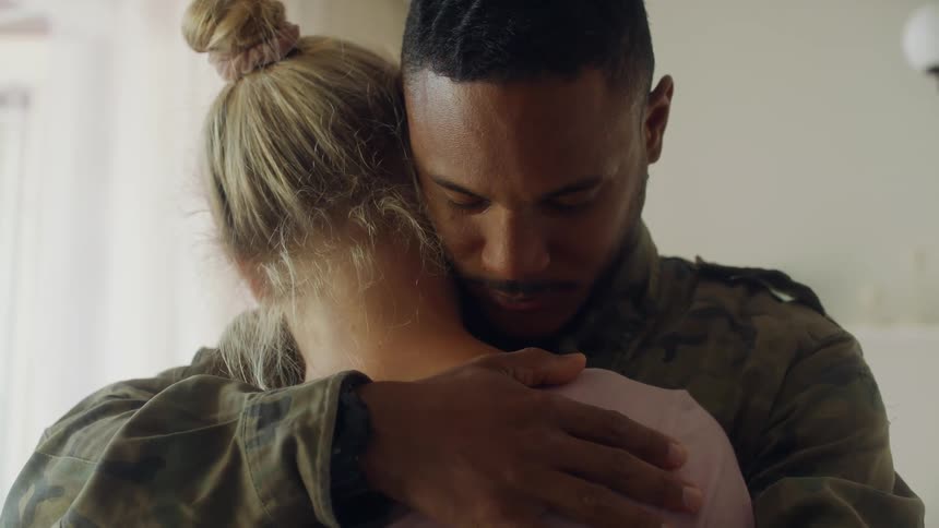 A male servicemember hugging a woman and rubbing her back