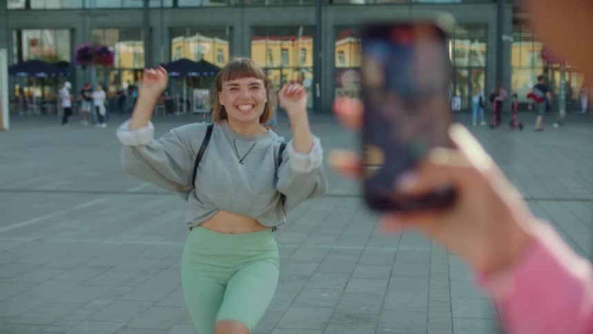 A girl films her friend dancing with a cell phone