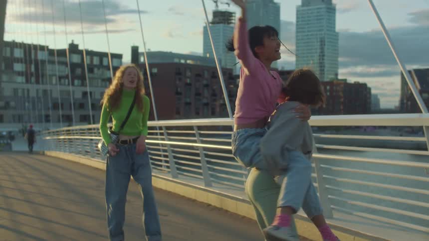 Friends walk next to rail over water laughing and smiling as one gives another woman a piggyback ride