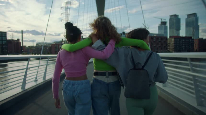 Three women walk while hugging on the bridge
