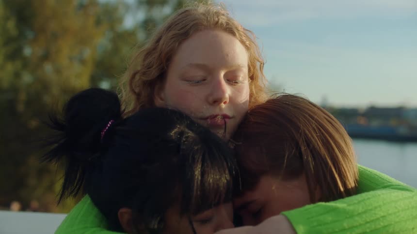 A group of young women share a group hug before waving goodbye to one member as she departs