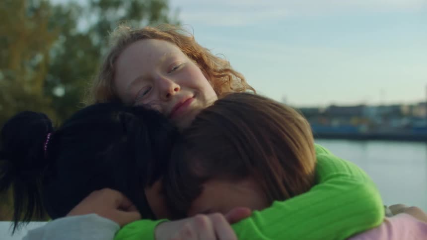 A young woman embraces two other women before waving goodbye as one departs