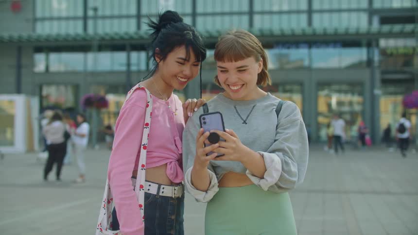Two women smile and take a selfie together by the building