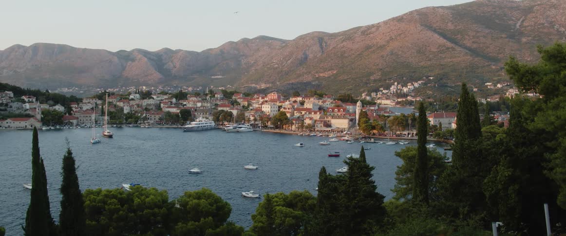 A lake with a marina with boats with buildings a mountain range the sky and clouds in the background
