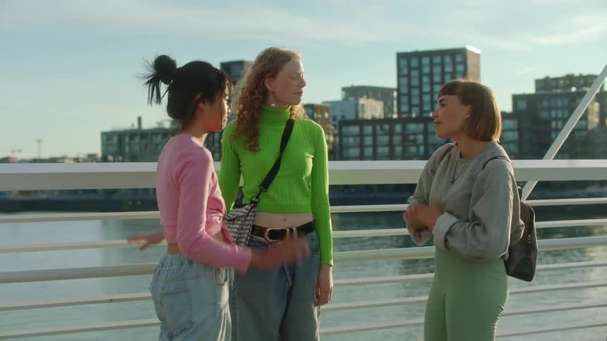 Three friends and say goodbye to one as they stand on a bridge over a river downtown