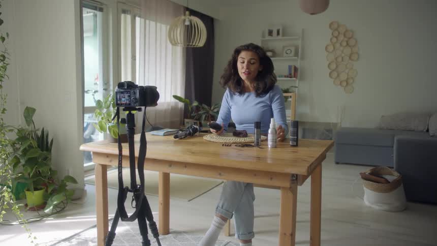 A woman filming herself using hair products while sitting at a table at home