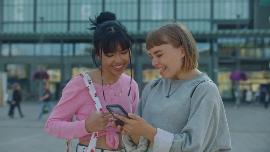 Two women outside smiling looking at a phone