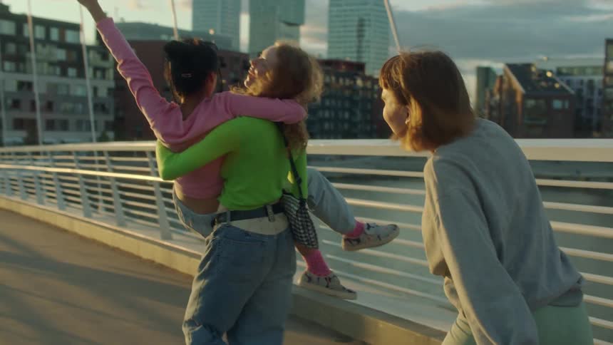 Two women are carrying another woman across a bridge in a city