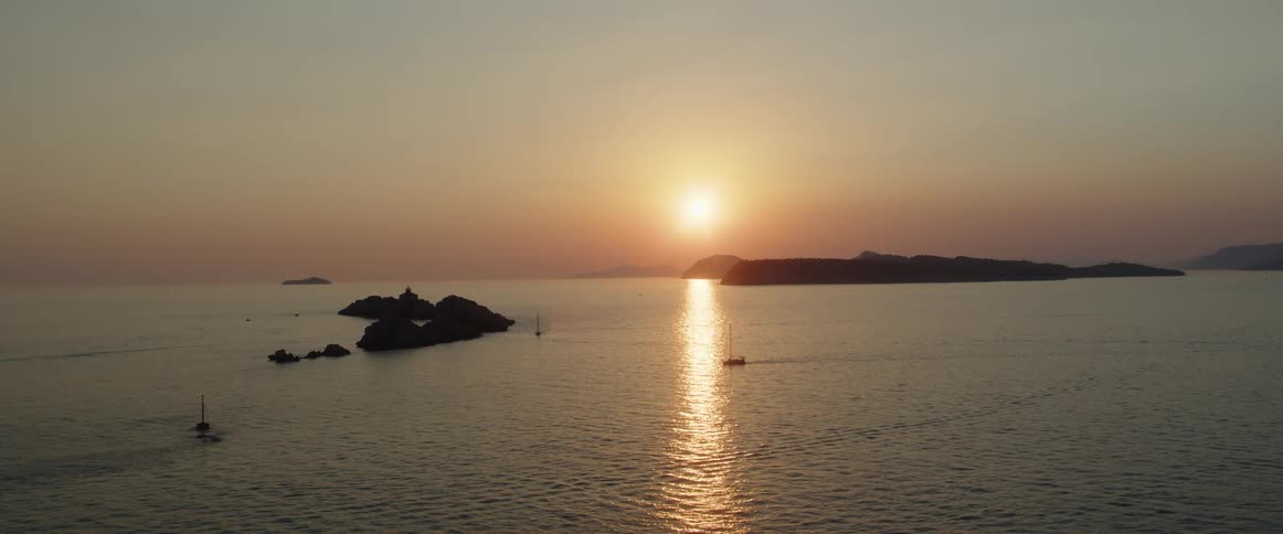 A boat sails as the sun sets over the ocean