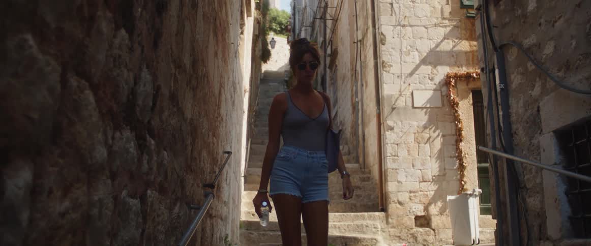 A woman is walking down stairs in a narrow passageway between buildings