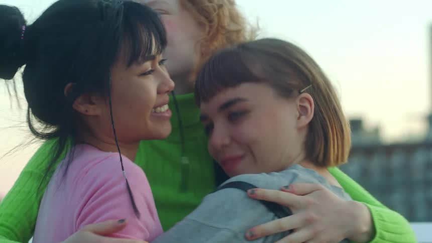 Two young women run toward their friend and hug her as they stand downtown