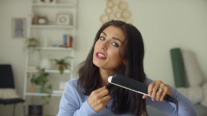 Woman discusses hair care while straightening her hair with an electric hair iron