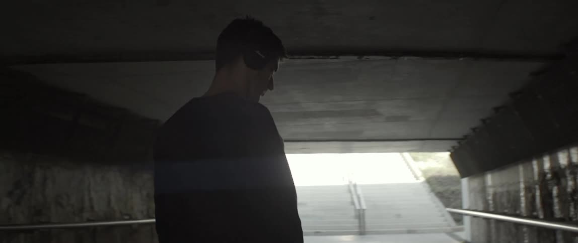 A man is standing under a dark overpass