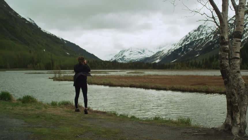 A woman walks to the stream and takes a photograph of the mountain range
