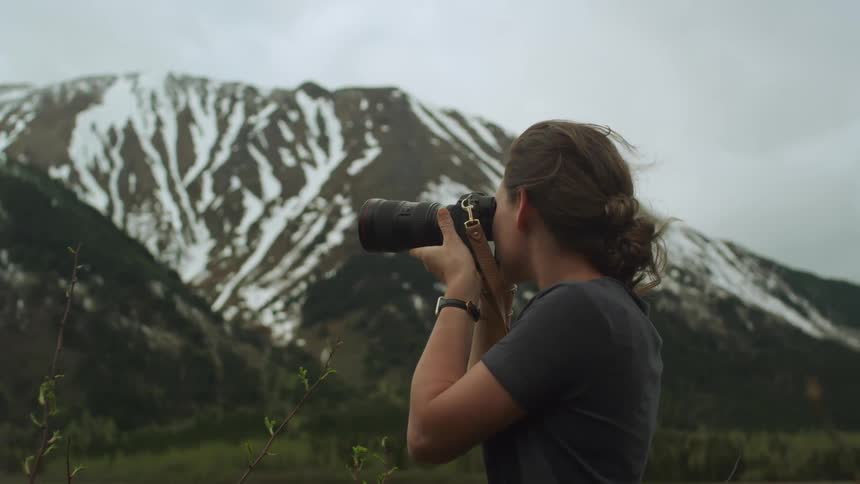 A woman takes photographs of a snow covered mountain under a cloudy sky