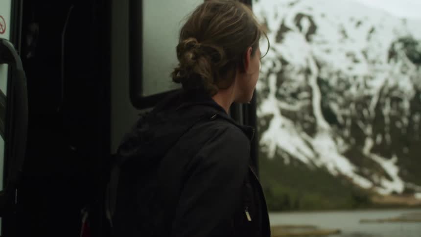 A woman steps out the back of a motorhome and walks toward nearby mountains