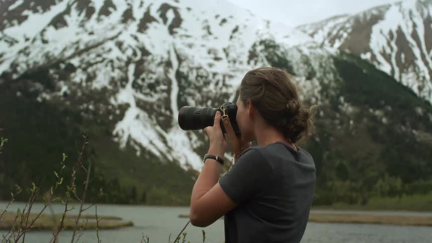 Young woman takes pictures of a lake near the mountains with a camera