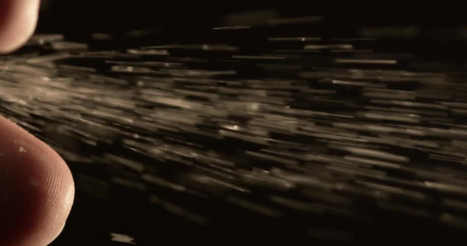 White grains streak away from fingers against dark background