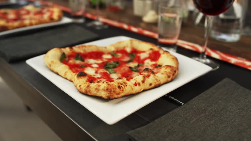 Freshly baked single serving pizza over a plate in a table on a restaurant