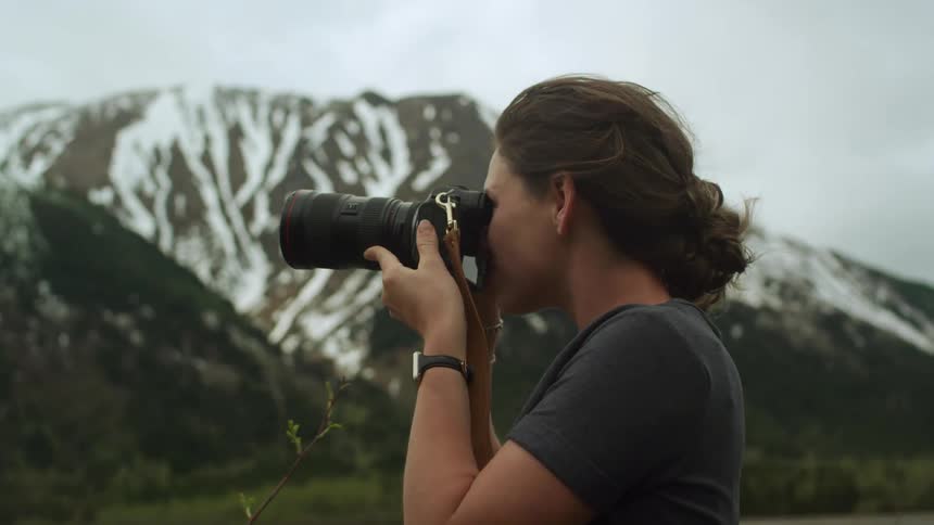 A photographer takes a photograph of a mountain range while standing in the countryside on a cloudy day