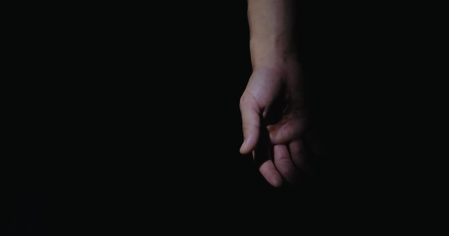 Human hand hanging down inside a dark room with black background