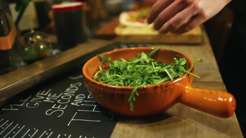 A person in a room taking a vegetable from a bowl on a table