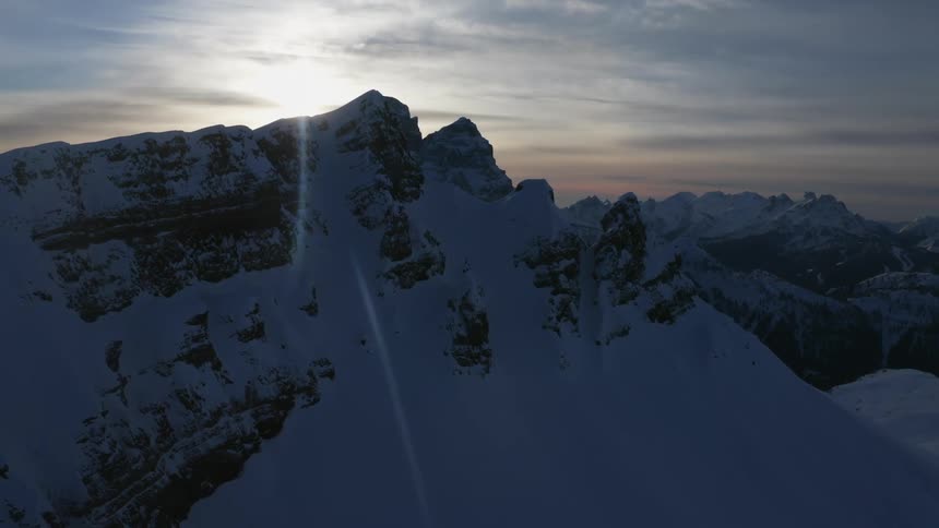 Sun shines from cloudy sky between snow covered mountain peaks
