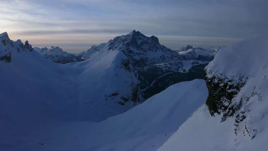 Snow covered mountains with peaks high in a cloudy sky as the sun is setting