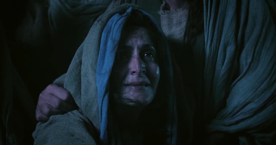 Woman wearing a hooded robe slowly slides down on her knees being held by others