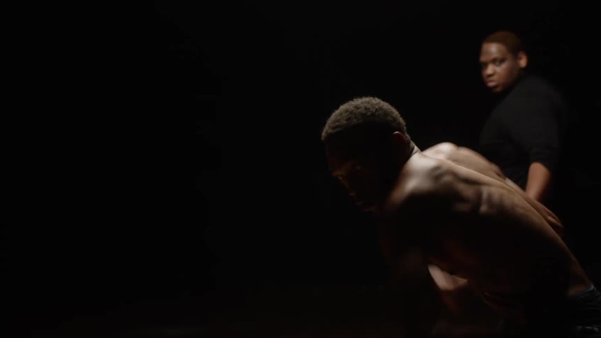 Young muscular shirtless man performing modern dance on a dark stage