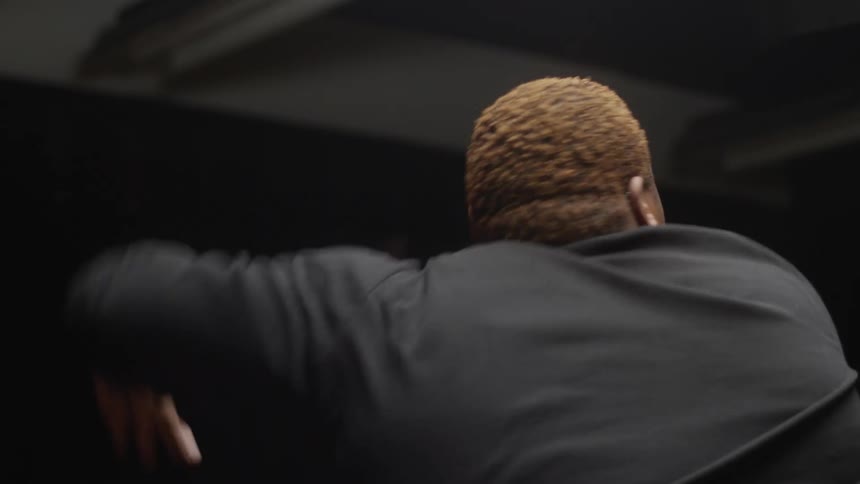 Man with short brown hair long black sleeve shirt dances in dark room doing arm moves