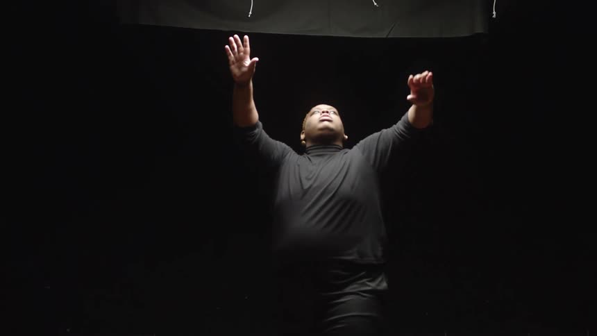 Man with earrings black sweatshirt and shorts dances in spotlight