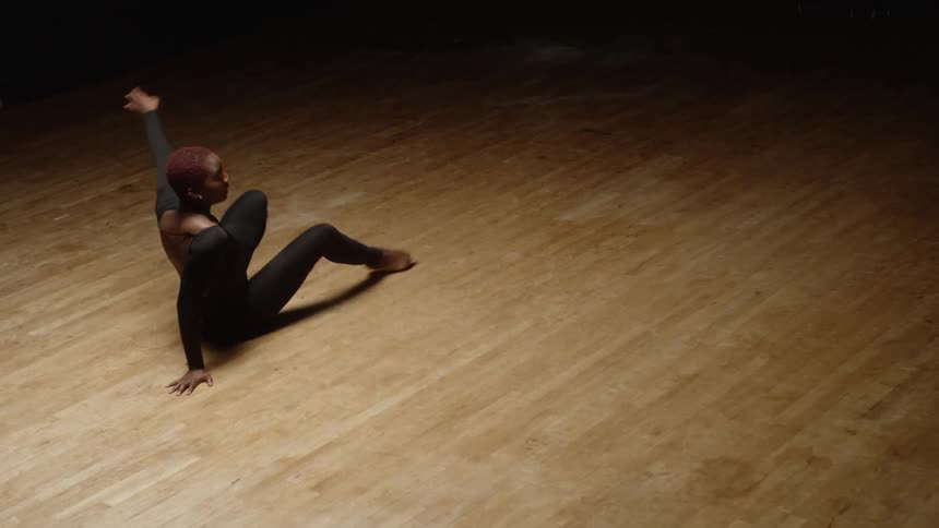 Woman wearing a thight black dress performing inerpretative dance over a wooden floor