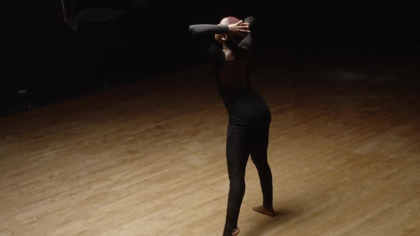 Young woman wearing thight dress performs interpretative dance over a wooden floor