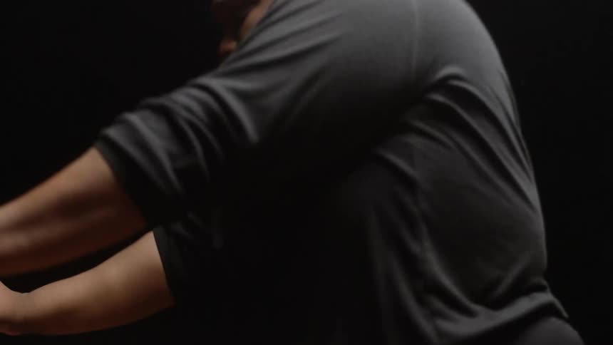 Male dancer wearing black turtle neck dances in dark room under stage light