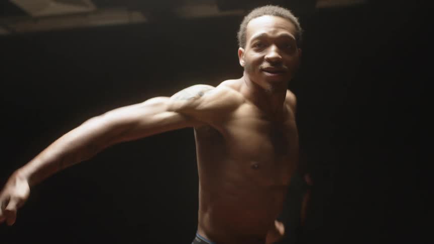 A man dances under a light in a dark dance studio