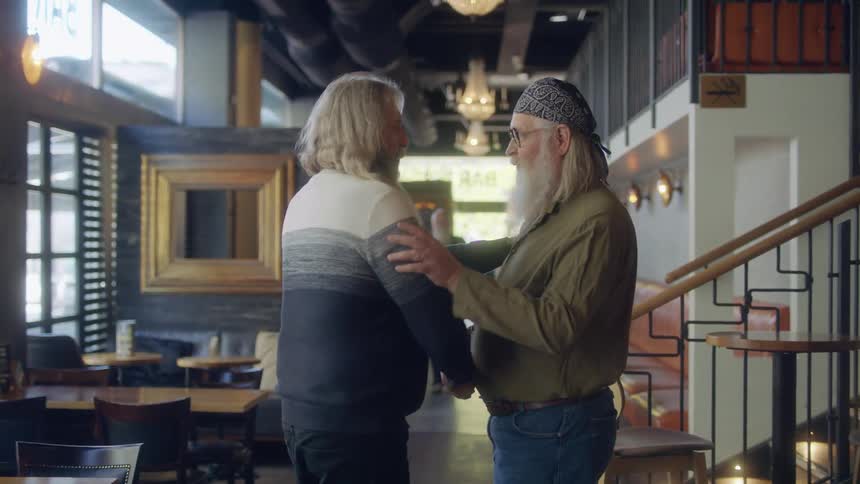 Two men greeting each other in a restaurant with chairs and tables in the background