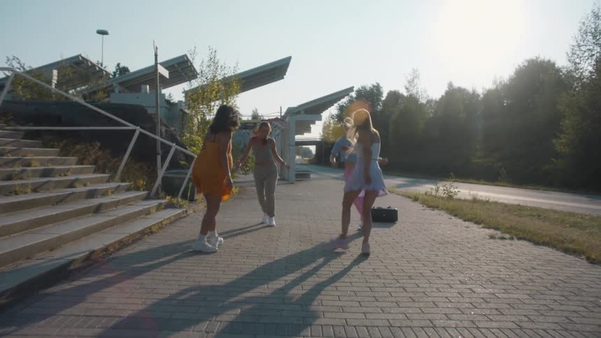 Four young women dance hip hop in a circle near a public trail