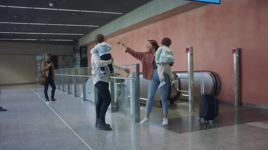 A family greets the mother as she gets off an escalator with her luggage