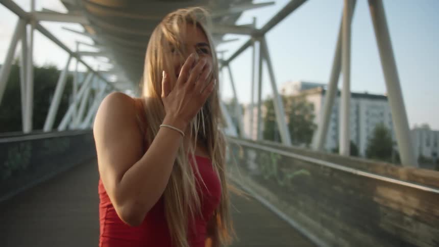Young woman wearing red dress laughing and talking on a bridge in the city at sunset